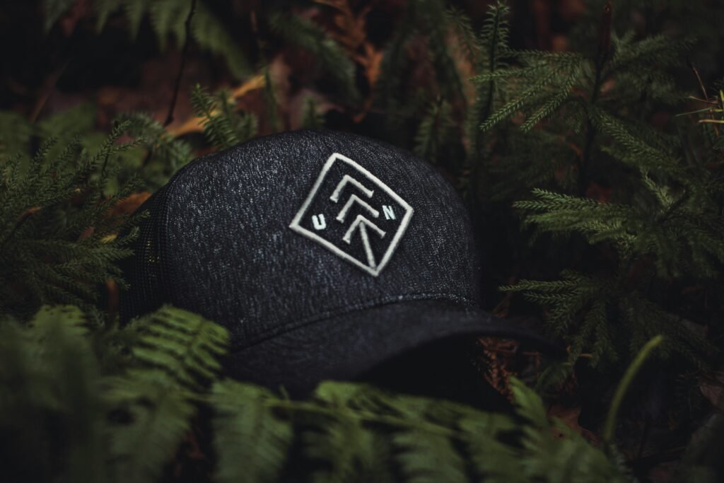 pexels-photo-1878821-1878821 Close-up of a dark baseball cap with an embroidered design nestled among green ferns, creating a nature-themed concept.